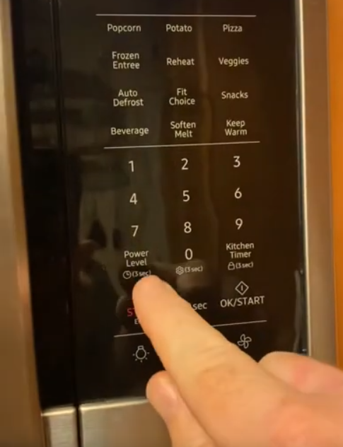 power button highlighted with finger on samsung microwave
